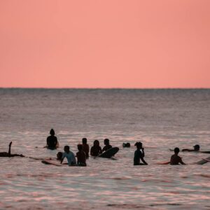 A group of surfers enjoying a peaceful sunset in Hawaii's warm ocean waters.