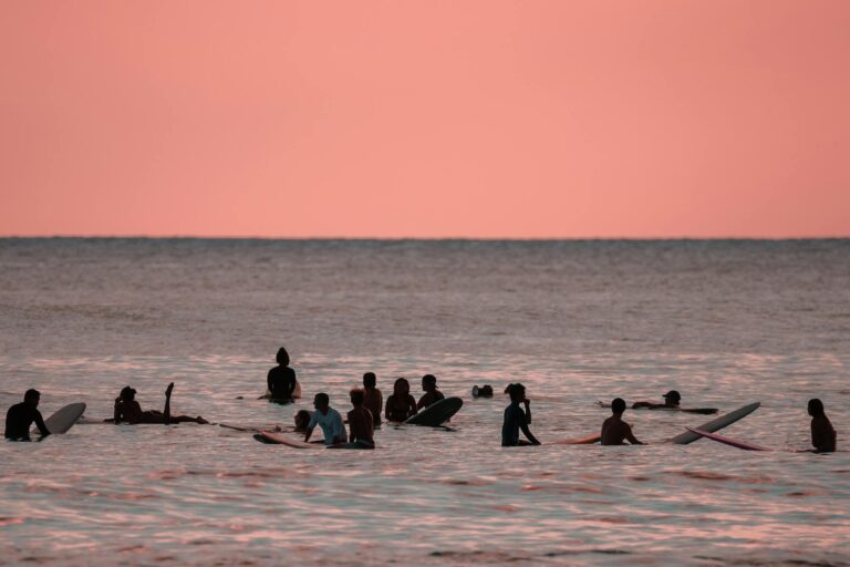 A group of surfers enjoying a peaceful sunset in Hawaii's warm ocean waters.