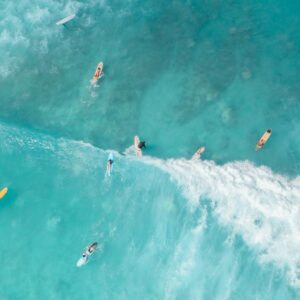 A group of surfers navigates crystal clear turquoise waves from an aerial perspective.