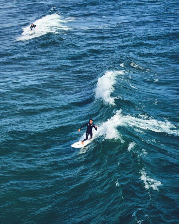 Aerial view of surfers navigating waves on a sunny day, capturing the essence of surfing.