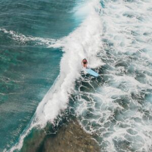 Drone shot capturing a surfer riding a wave in the clear blue waters of Hawaii.