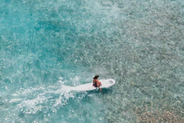 Drone shot of a surfer in crystal clear waters of Hawaii. Surfing and ocean adventure captured beautifully.