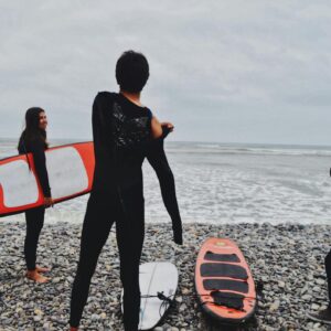 Group of surfers in wetsuits preparing by the ocean with surfboards on a rocky beach.