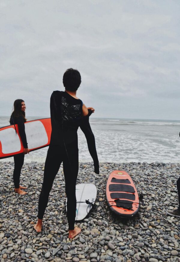 Group of surfers in wetsuits preparing by the ocean with surfboards on a rocky beach.